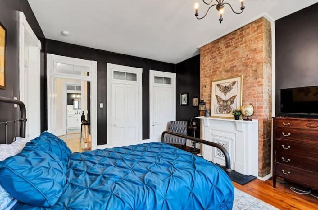 A bedroom with a large bed, a fireplace, a TV, and a brick accent wall.