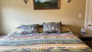 A bedroom with a large bed, a painting of a mountain, and two wall sconces.
