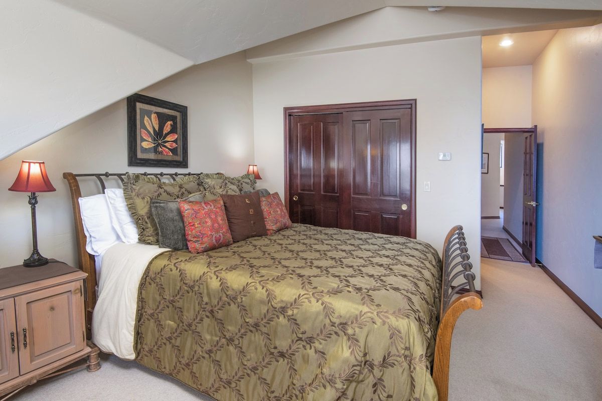 A bedroom with a bed, a nightstand, a lamp, a door, and a framed picture on the wall.