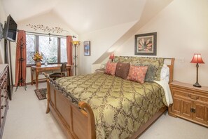 A bedroom with a bed, a desk, a chair, a dresser, a television, and a window with curtains.