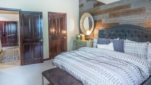 Quarto com cama grande, cabeceira de madeira, mesa de cabeceira com abajur e espelho.