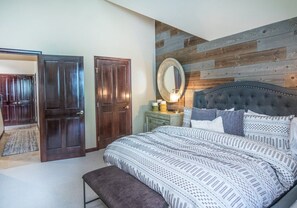 A bedroom with a large bed, a wooden headboard, a nightstand with a lamp, and a mirror. - Charlie's Slopeside: Arrowhead Ski-In/Out, Steps to Lift, Sleeps 8, Heated Pool + Hot Tub (Edwards)