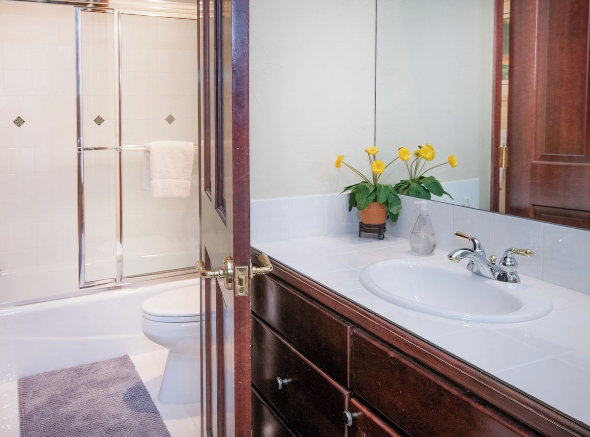 A bathroom with a glass-enclosed shower, a white sink with a mirror, and a potted plant with yellow flowers.