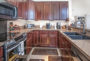 A kitchen with dark wooden cabinets, stainless steel appliances, a built-in oven, and a double sink. - Charlie's Slopeside: Arrowhead Ski-In/Out, Steps to Lift, Sleeps 8, Heated Pool + Hot Tub (Edwards)