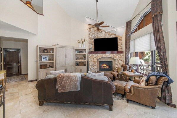 A spacious living room with a fireplace, leather sofas, and a television mounted on the wall.