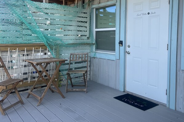 A wooden deck with a table and chairs, a white door with a window, and a welcome mat.