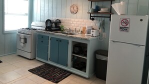A kitchen with teal cabinets, a white stove, a sink, and a refrigerator. There is a clock on the wall and a 'No Smoking' sign on the refrigerator.
