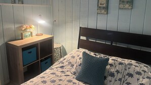 A bedroom with a wooden bed, a bedside table with a lamp, and wall decorations including fish and shells.