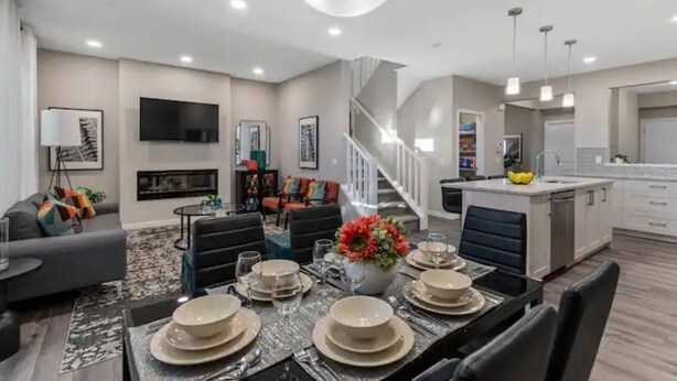 A modern living room with a dining area set for six, a staircase, and a kitchen area.