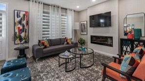 A modern living room with a grey sofa, two round coffee tables, and a TV mounted on the wall.