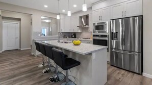 A modern kitchen with a central island, stainless steel appliances, and bar stools.