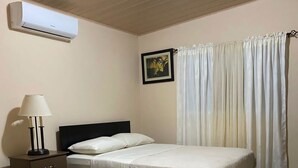 Un dormitorio con dos camas, una mesita de noche, una lámpara, aire acondicionado e iluminación en el techo.