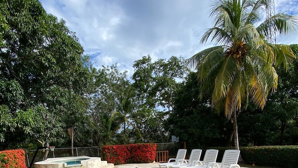 Una piscina rectangular con agua azul cristalina, rodeada por un solárium de hormigón. Hay tumbonas blancas alineadas a lo largo del borde de la piscina.