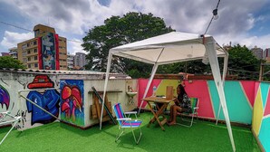 Un patio en la azotea con césped artificial, un toldo blanco, grafitis de colores y una silla metálica.