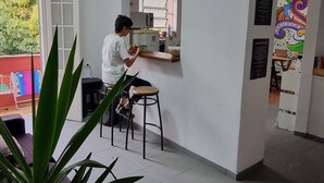 Una cocina moderna con una persona preparando comida en una encimera. Hay una ventana con persianas, un refrigerador y un lavabo.