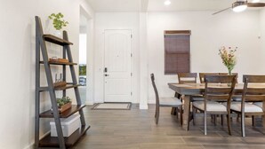 A dining area with a wooden table and chairs, a ladder shelf with plants, and a white door. - Luxury Home in Litchfield Park w/Free Pool Heating (Litchfield Park)