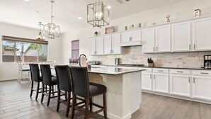 A modern kitchen with white cabinetry, a large island, and pendant lighting. - Luxury Home in Litchfield Park w/Free Pool Heating (Litchfield Park)