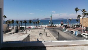 Vista costanera amb una estàtua, palmeres i un cel serè.