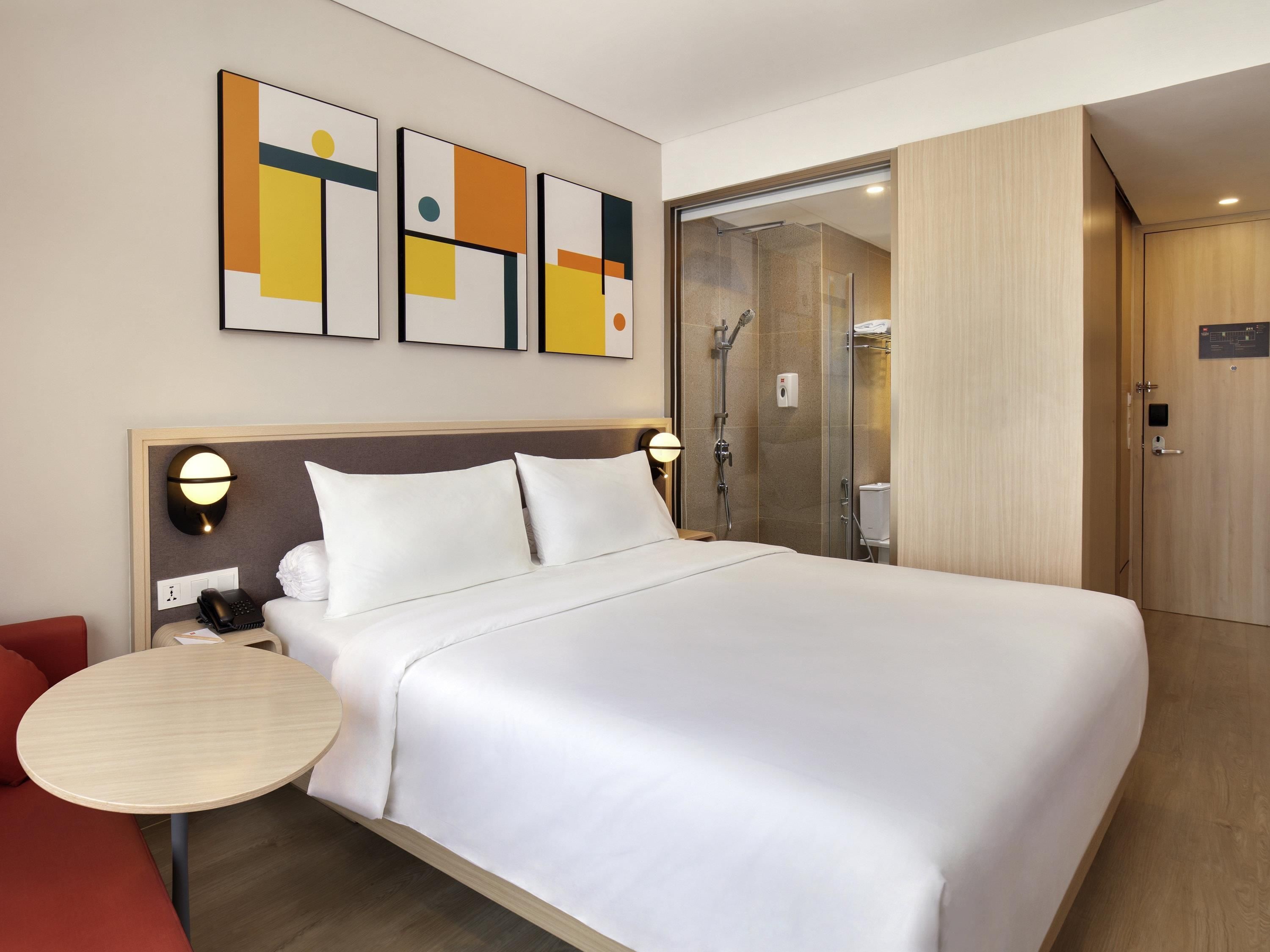 A hotel room with a large bed, bedside tables, a shower, and artwork on the wall.
