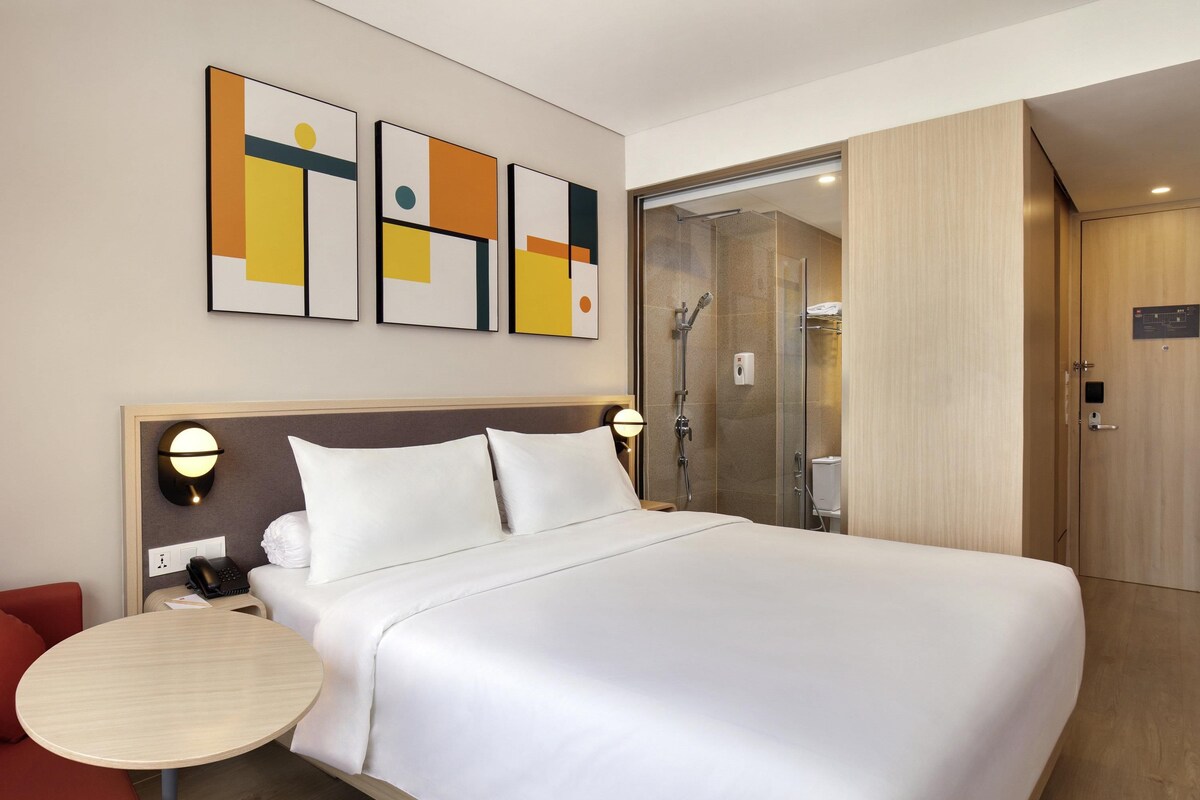 A hotel room with a large bed, bedside tables, a shower, and artwork on the wall.