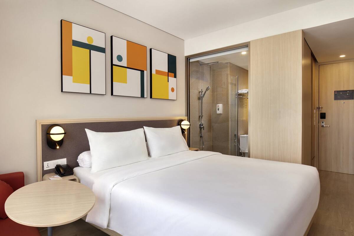 Quarto de hotel com uma cama grande, mesas de cabeceira, chuveiro e obras de arte na parede.