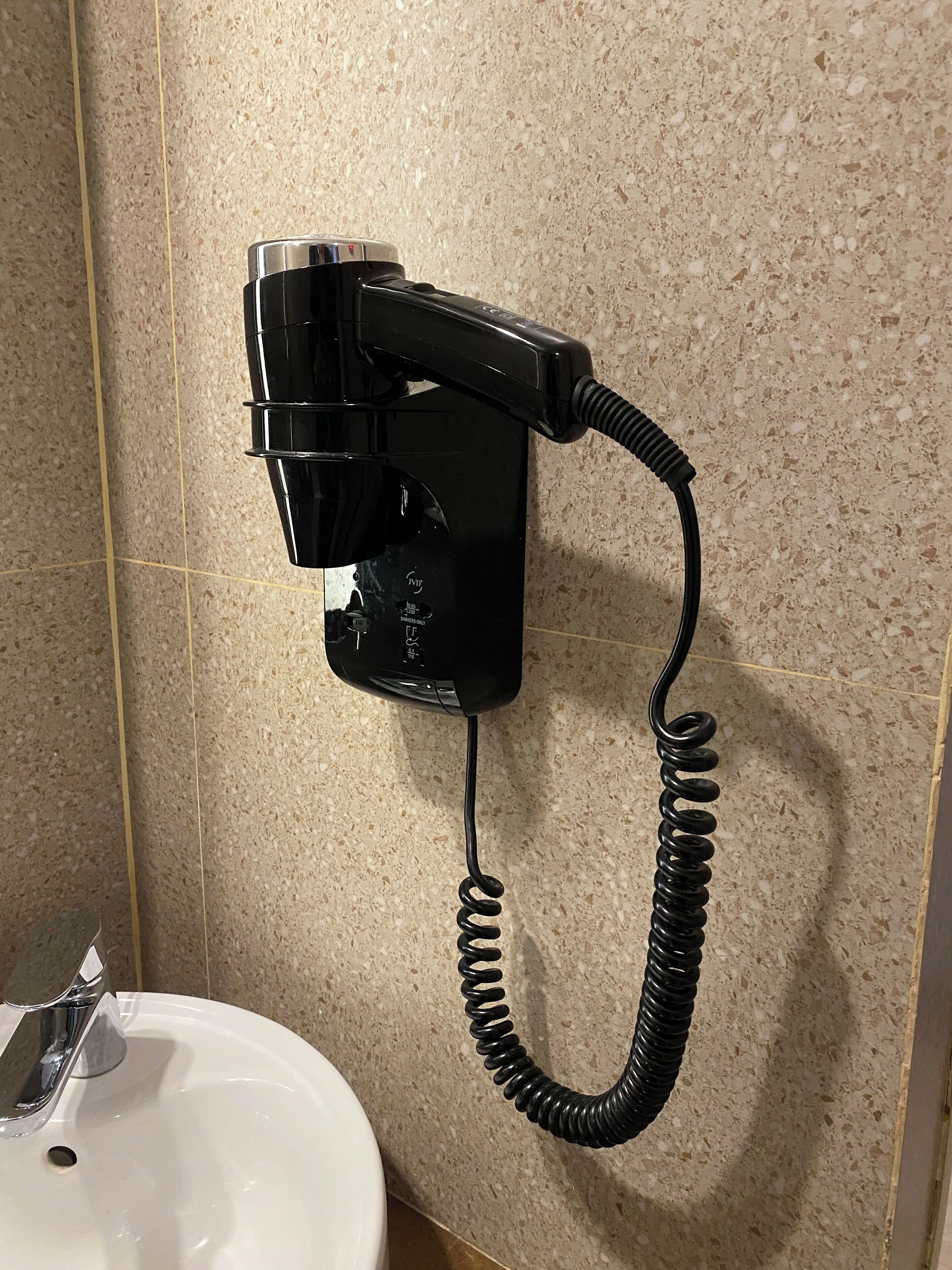 Un sèche-cheveux fixé au mur dans une salle de bain équipée d’un lavabo.
