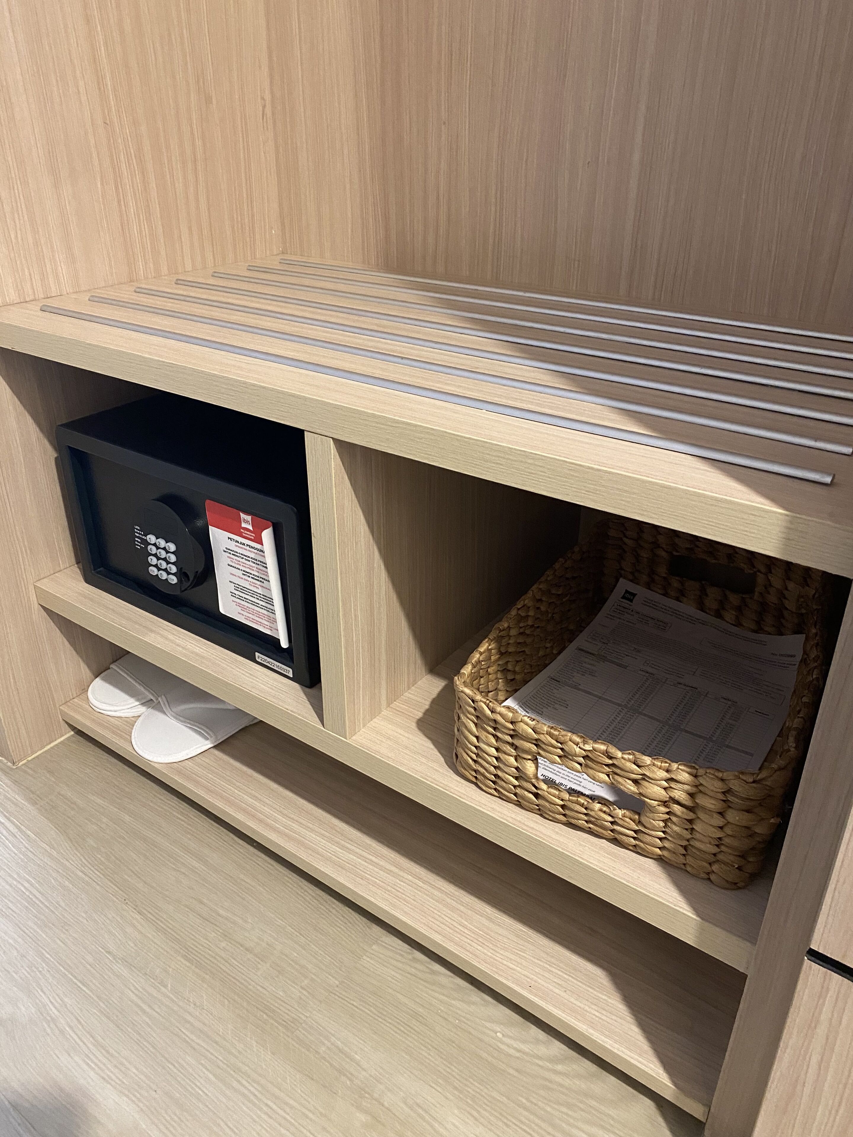 A wooden shelf with a black electronic device, a white shoe, and a woven basket with a receipt.