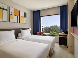Habitación de hotel con dos camas, televisión, una mesita y ventana con cortinas.