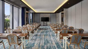 A conference room with rows of tables and chairs, a large flat-screen TV, and a patterned carpet.
