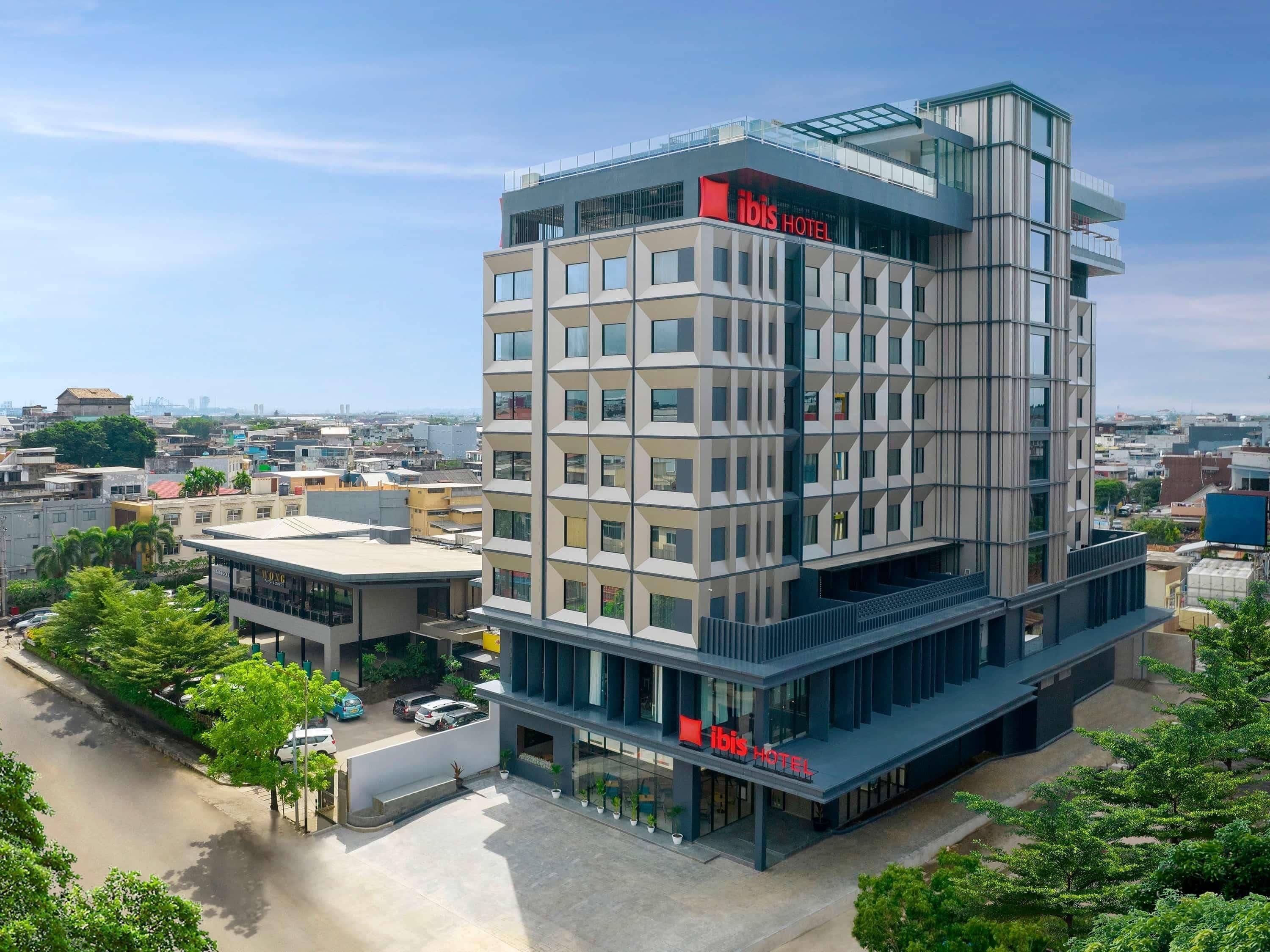 A modern hotel with a prominent 'ibis HOTEL' sign, multiple floors, and a glass facade.