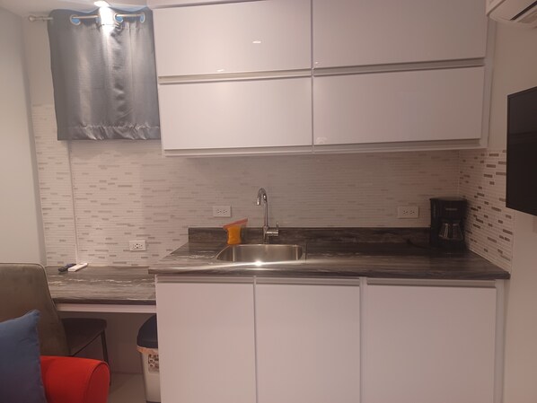 Una cocina compacta con gabinetes blancos, un lavamanos de acero inoxidable y una cafetera.