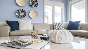 A living room with a sofa, cushions, a coffee table, a book, a beaded necklace, and wall decorations.