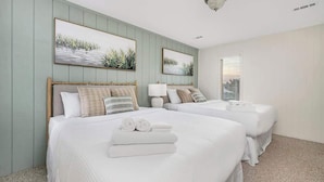 A hotel room with two beds, a large window with blinds, and artwork on the wall.