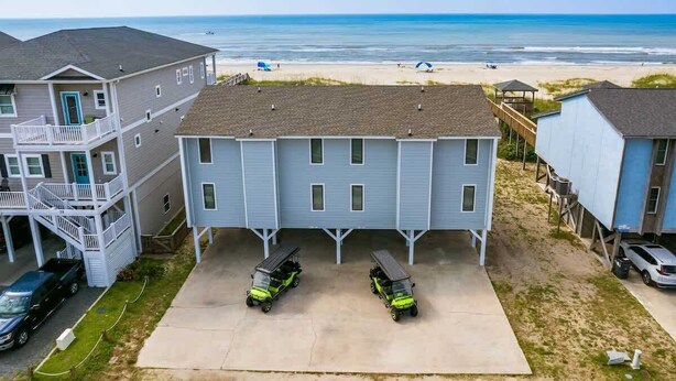 A two-story building with a covered parking area and a view of the beach.