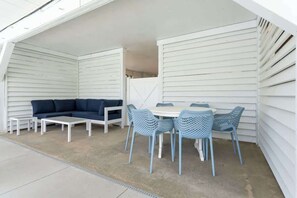 An outdoor patio with a white sofa, a round table, and blue chairs.
