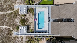 An aerial view of a hotel with a swimming pool, lounge area, and a beach access path.