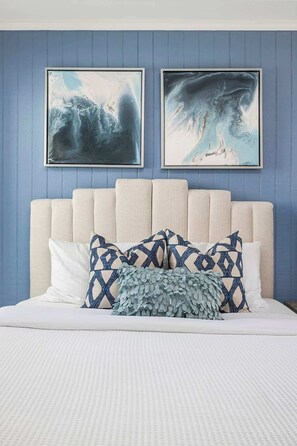 A bedroom with a bed, two framed artworks, and a headboard.
