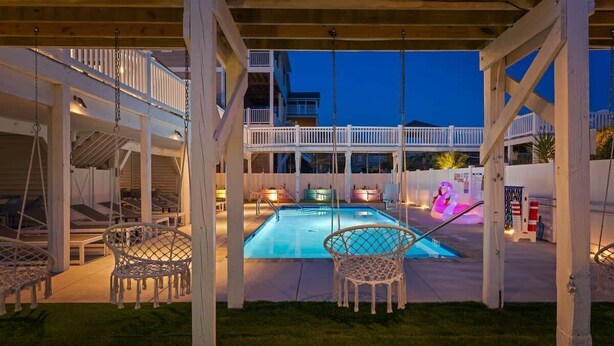 Ein überdachter Poolbereich mit Holzterrasse, weißen Geländern und einer Liege am Pool.
