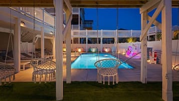 A covered outdoor pool area with a wooden deck, white railings, and a poolside chair.