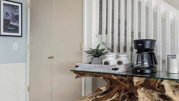 A dining area with a glass-top table featuring a natural wood base, a coffee maker, and a potted plant.