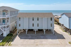 A beachfront property with a two-story building, a covered parking area, and a view of the ocean. - Oceanfront, Pool, GolfCart, & Free EV Charger! (Ocean Isle Beach)