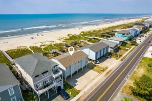 A coastal residential area with beachfront properties, a road with a bike lane, and a pier in the distance. - Oceanfront, Pool, GolfCart, & Free EV Charger! (Ocean Isle Beach)