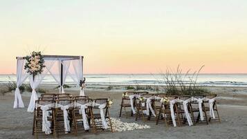 A beach wedding setup with wooden chairs and a white canopy.