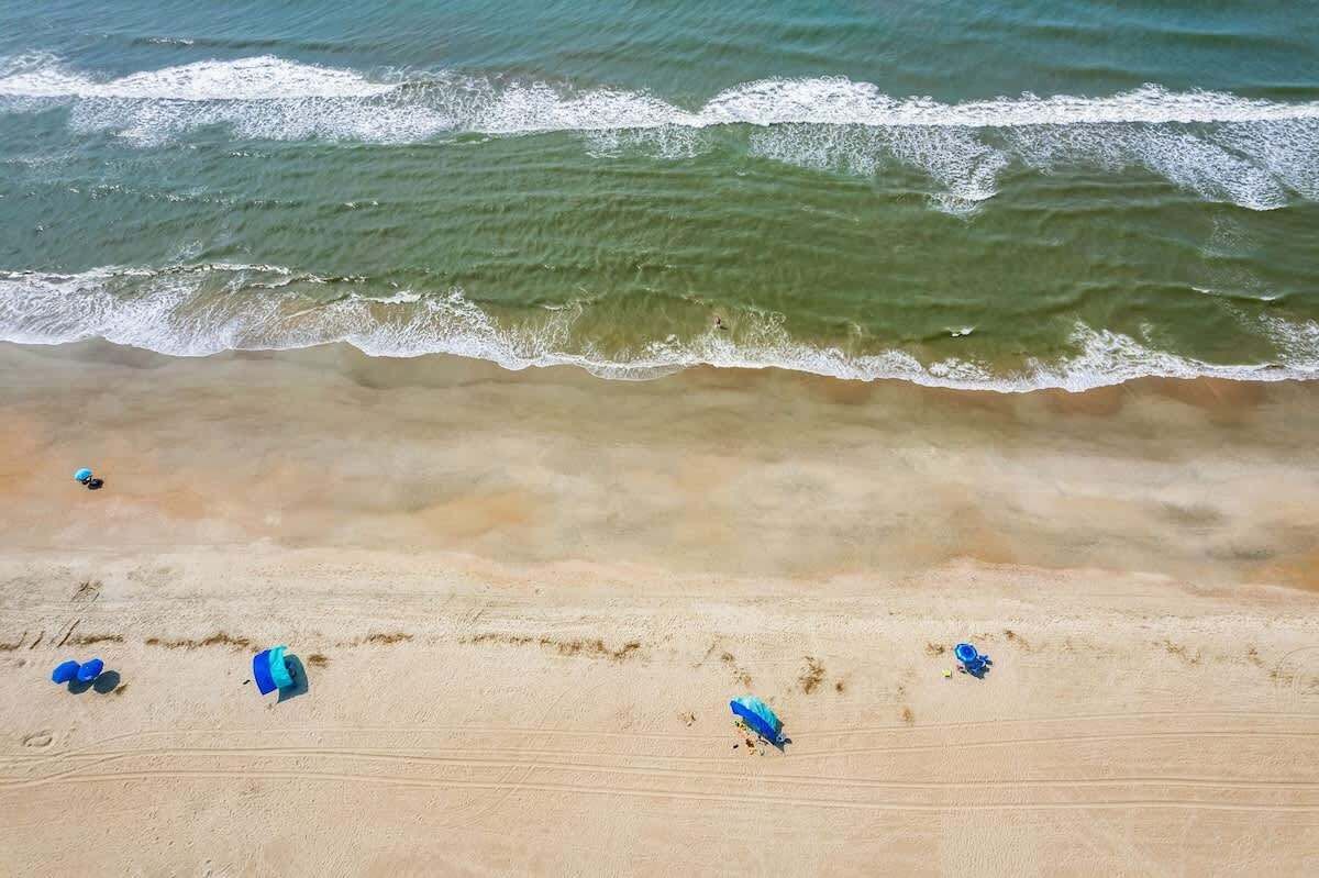 A beach with waves approaching the shore and several blue umbrellas scattered on the sand.