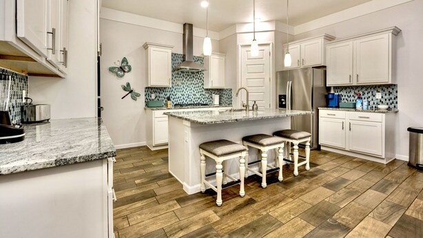 Una cucina moderna con mobili bianchi, un'isola centrale con sgabelli, un frigorifero in acciaio inossidabile e uno schienale decorato con un motivo blu e bianco.