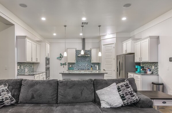 A modern kitchen with white cabinets, a gray sofa, and pendant lights.