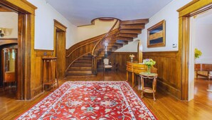 Un magnifique escalier en bois, doté de rampes et recouvert d’un tapis rouge à motifs, menant à un palier.