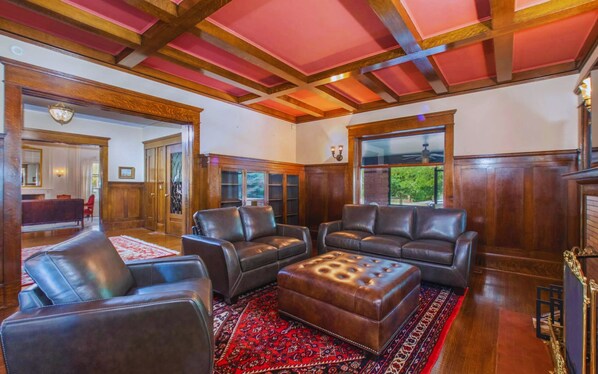 A spacious living room with leather sofas, a patterned rug, and wooden paneling. - Whole 9BR Historic Mansion, Weddings & Events (Lincoln)