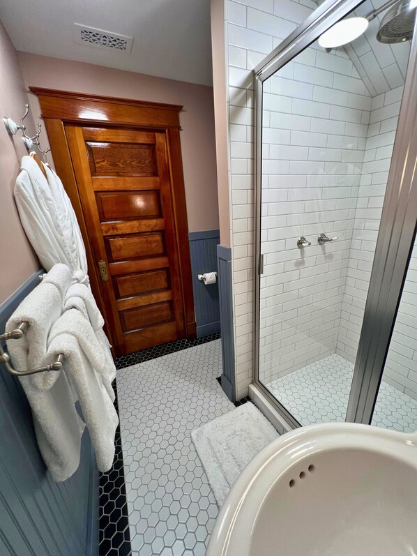 A bathroom with a glass-enclosed shower, a wooden door, and a towel rack with white towels.