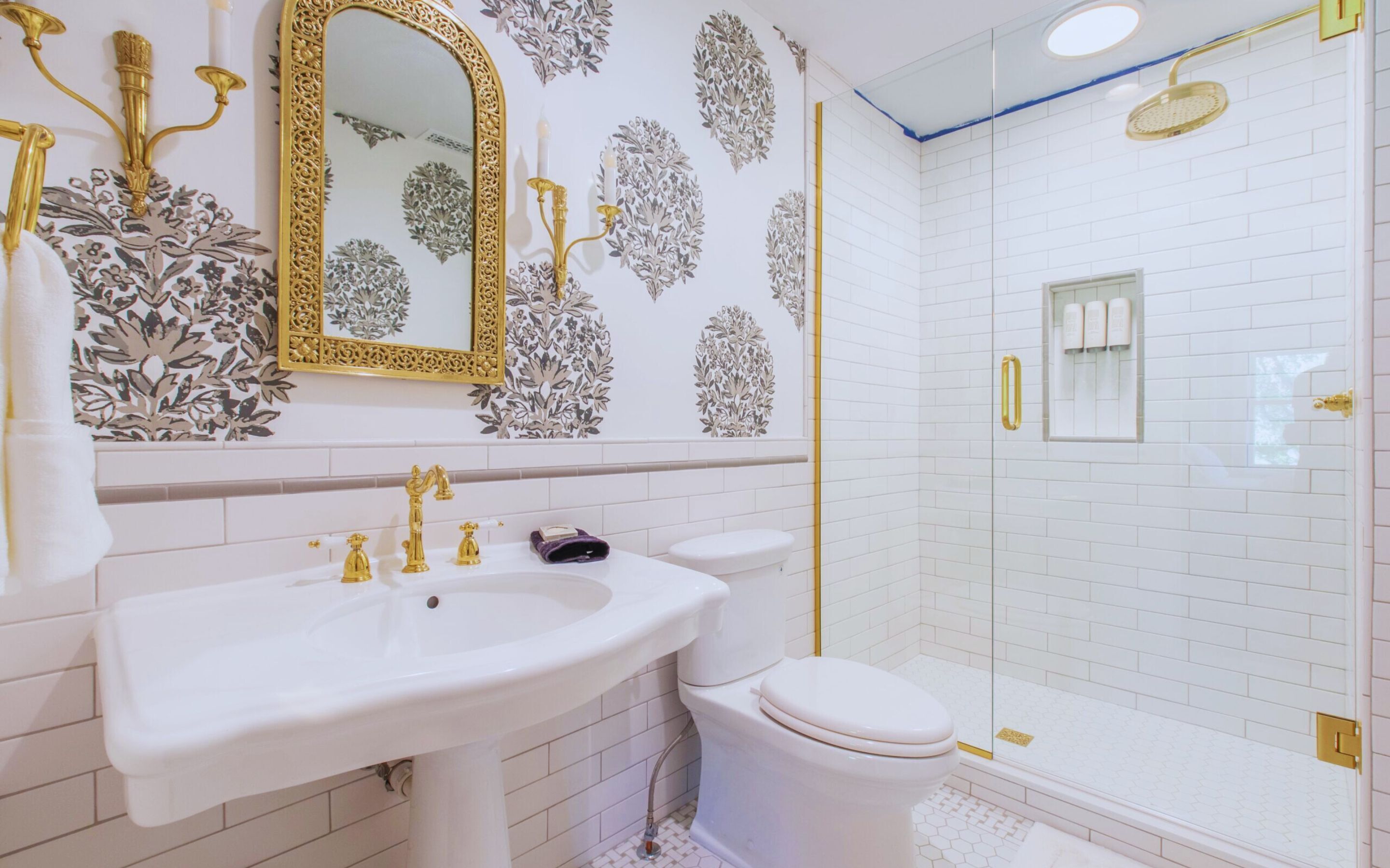 Een badkamer met een wit wastafelmeubel, gouden accessoires, een toilet en een douche met een glazen deur.